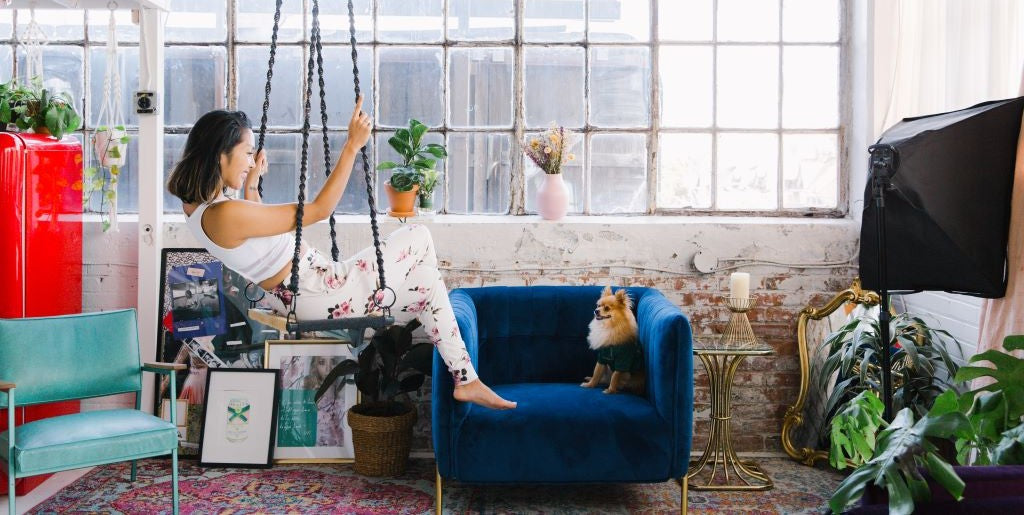 Woman sitting on a swing in a stylish living room with a dog on a blue couch.